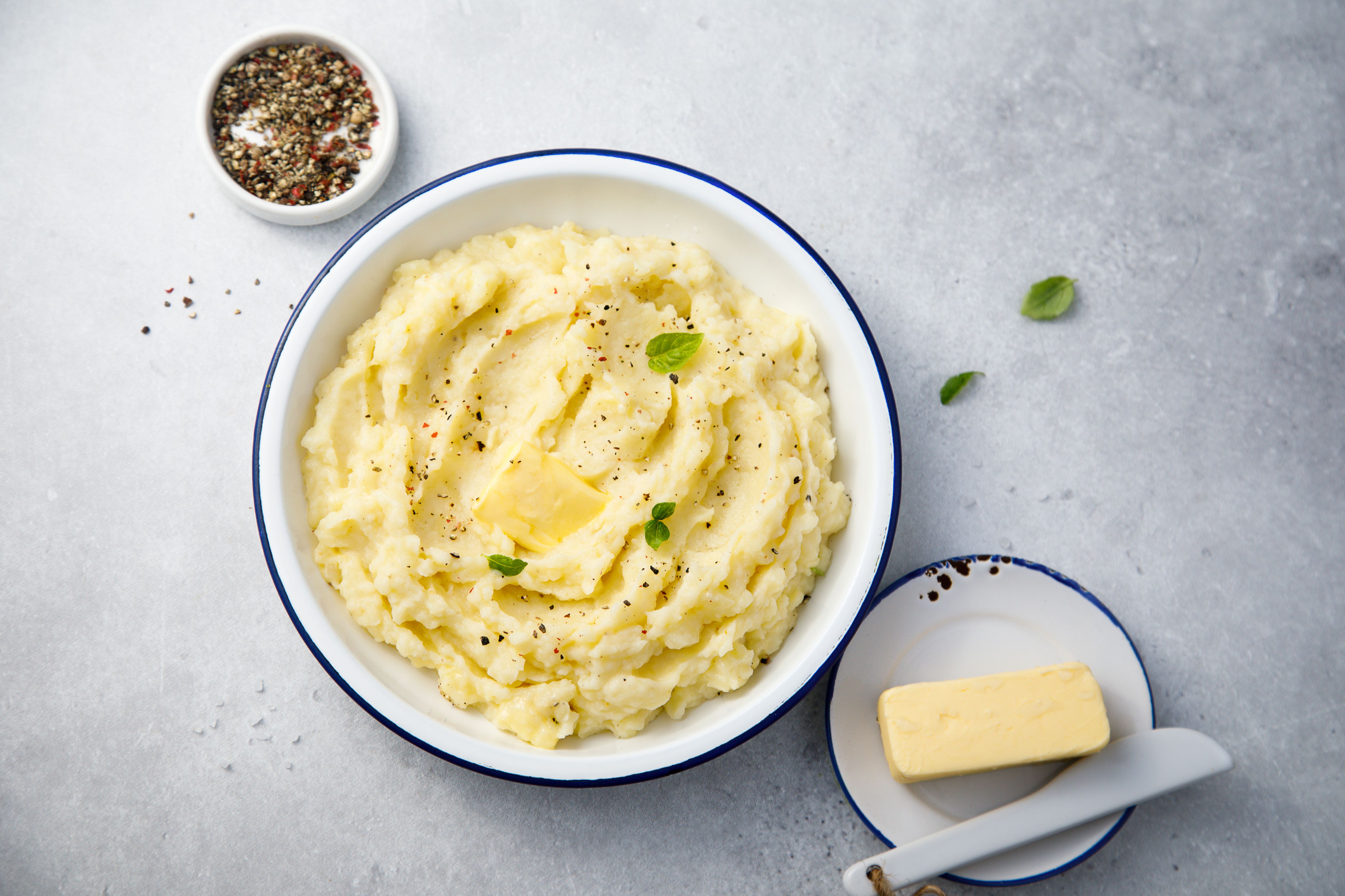Schale Kartoffelpüree mit schmelzender Butter und Kräutern, daneben Butter und Pfeffer