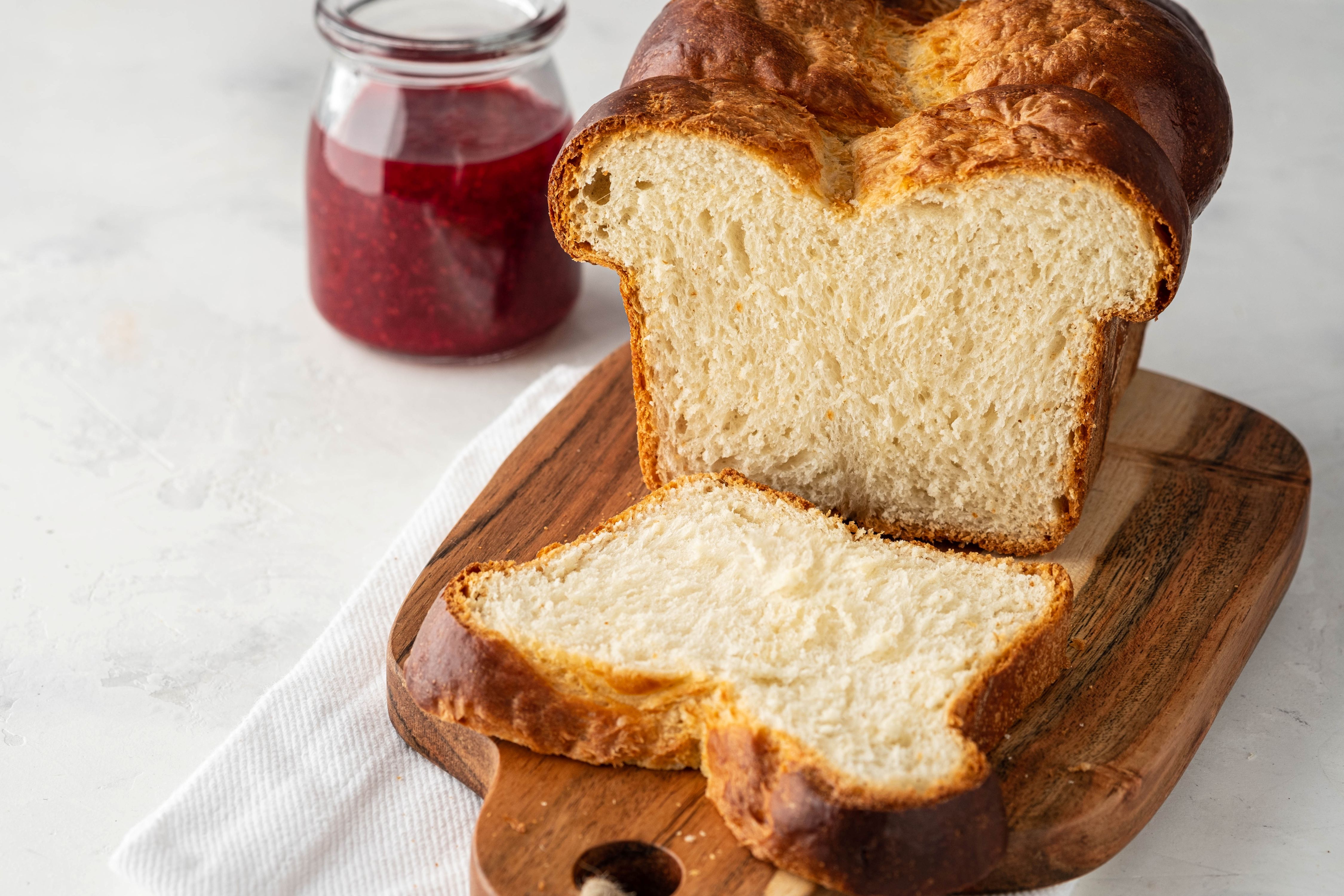 Angeschnittener Brioche-Laib auf einem Holzbrett mit einem Glas Marmelade