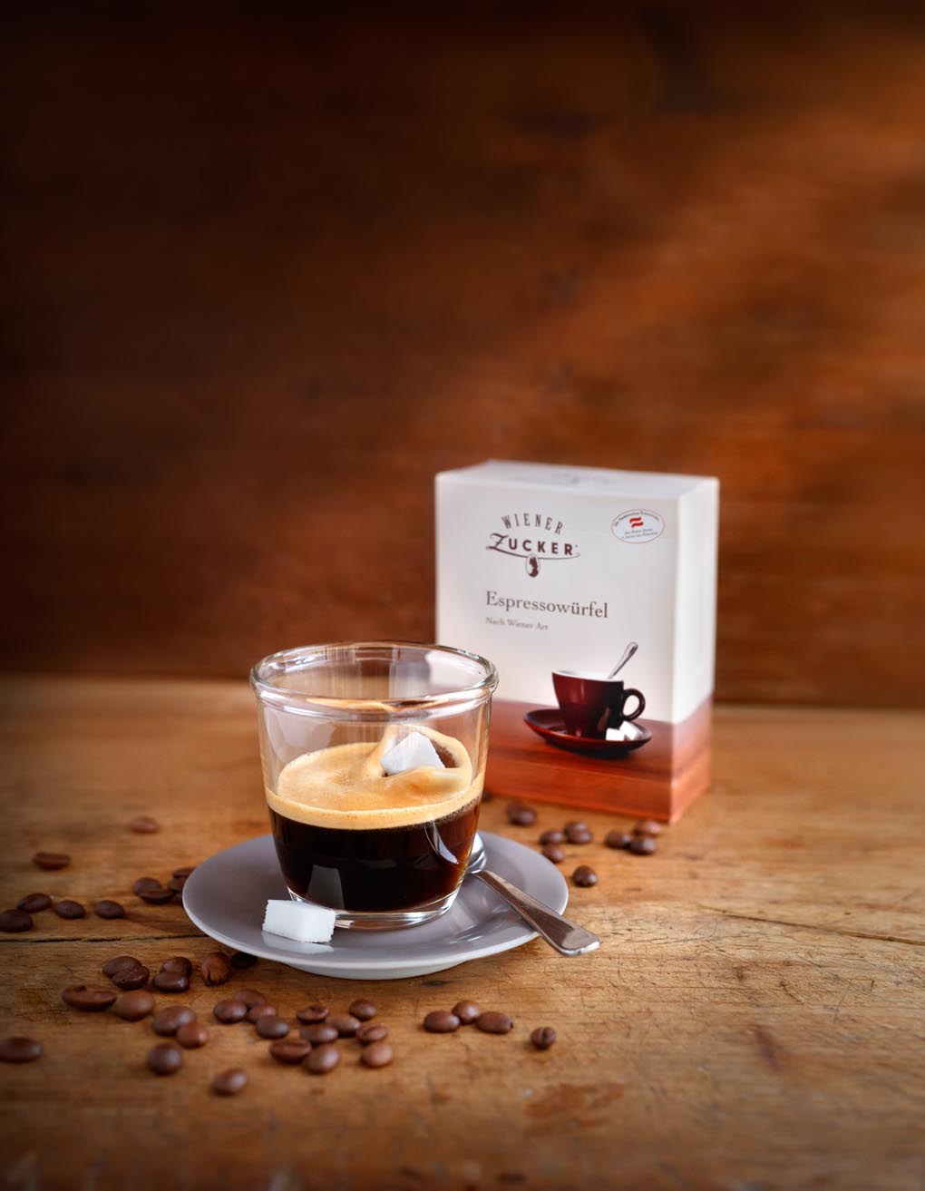 Glass of espresso with a sugar cube next to a pack of Wiener Zucker Espressowürfel on a wooden table