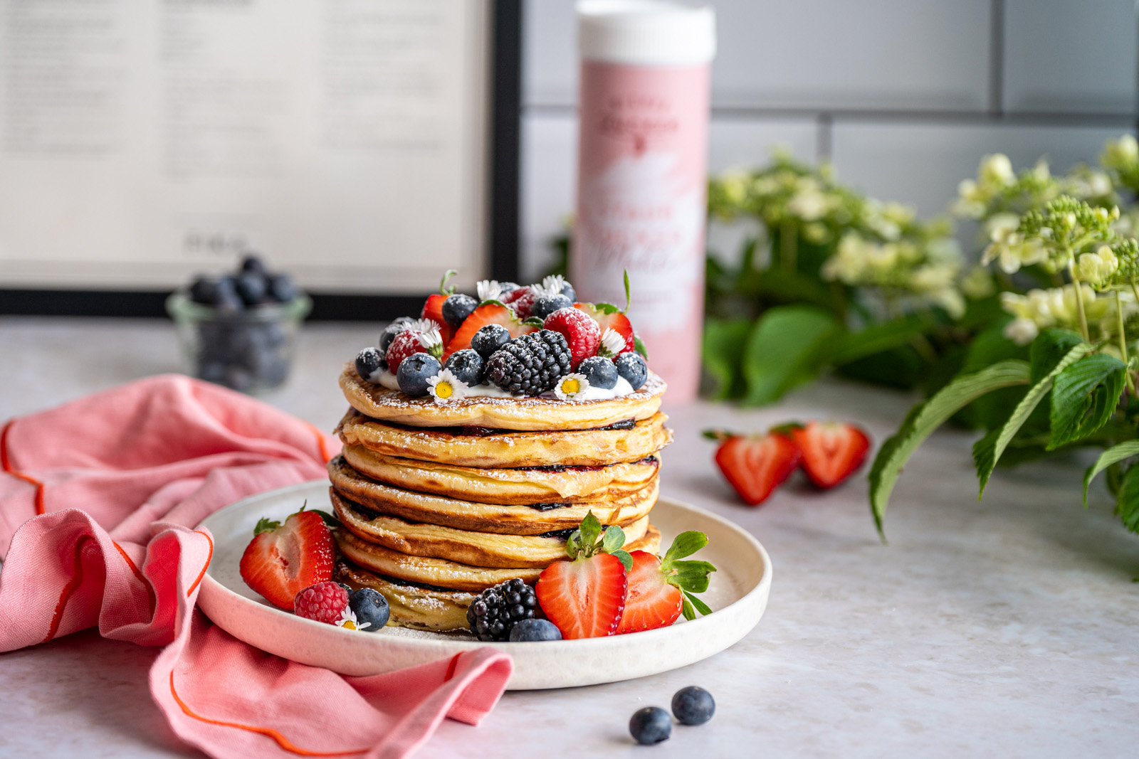 Stack of pancakes topped with berries and dusted with powdered sugar, a pink sugar shaker in the background [no AI]