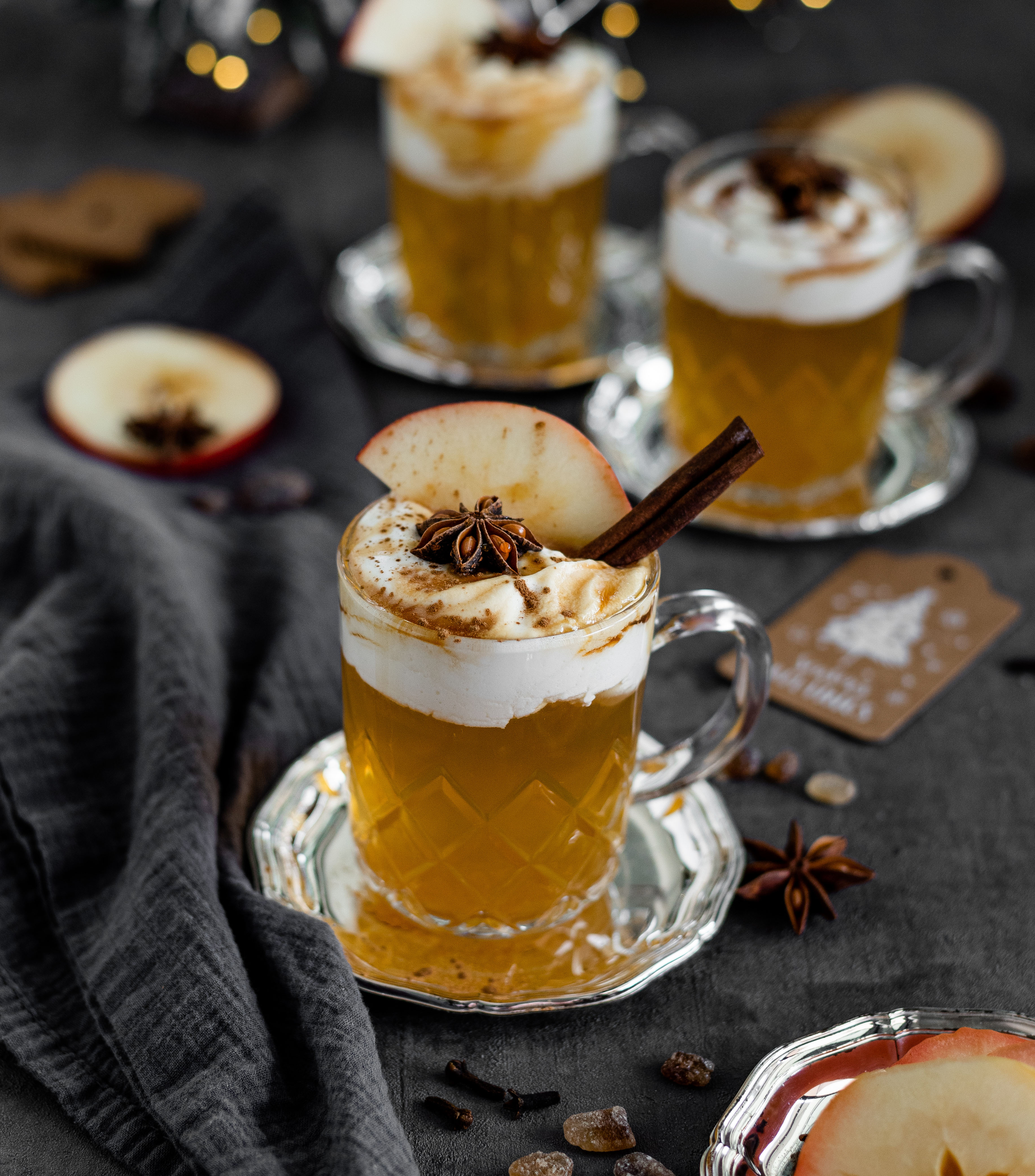 Hot mulled cider in glass mugs with whipped cream, apple slices, star anise and cinnamon sticks