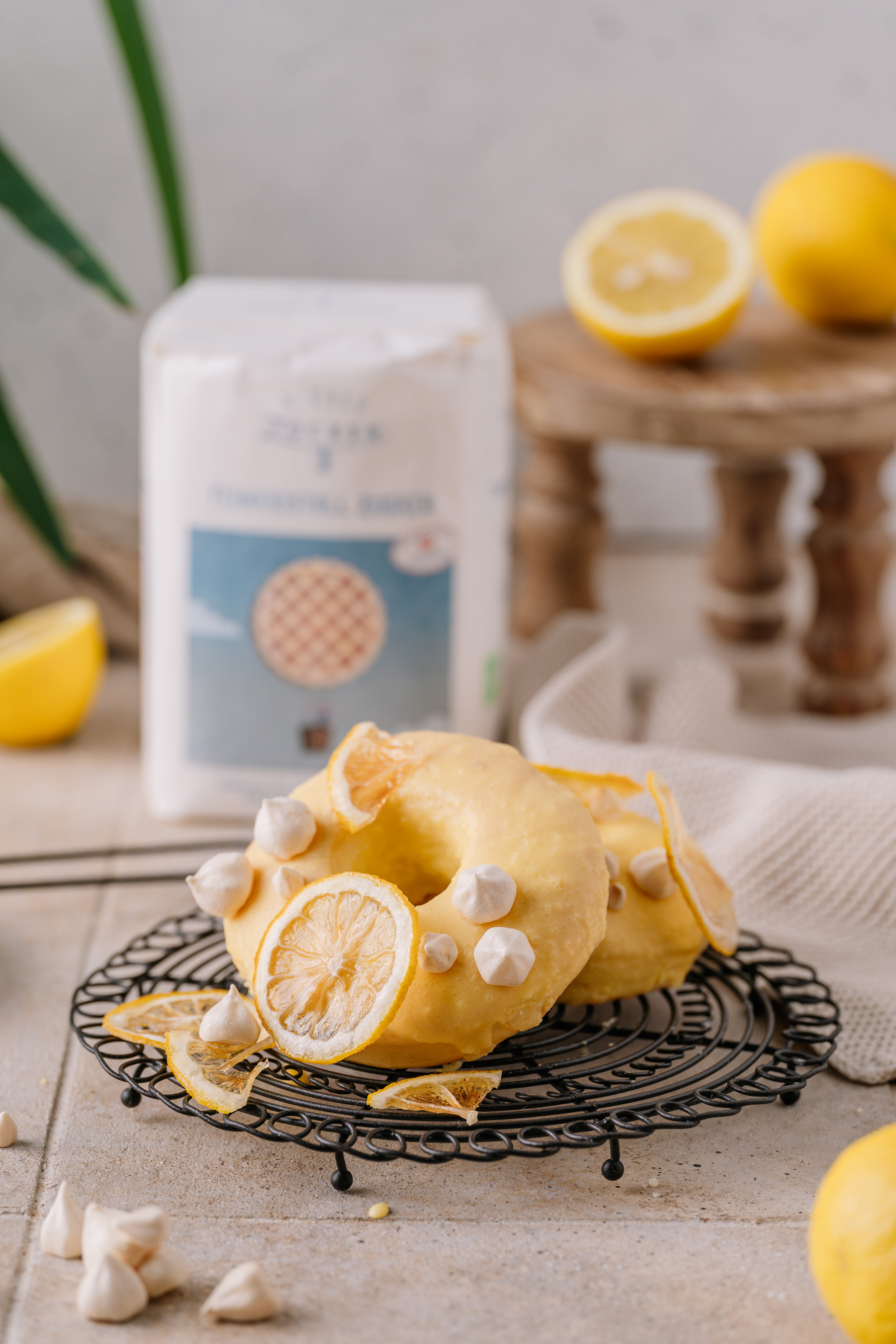 Lemon-glazed donuts with dried lemon slices and meringue on a rack, a pack of Wiener Zucker Feinkristall behind