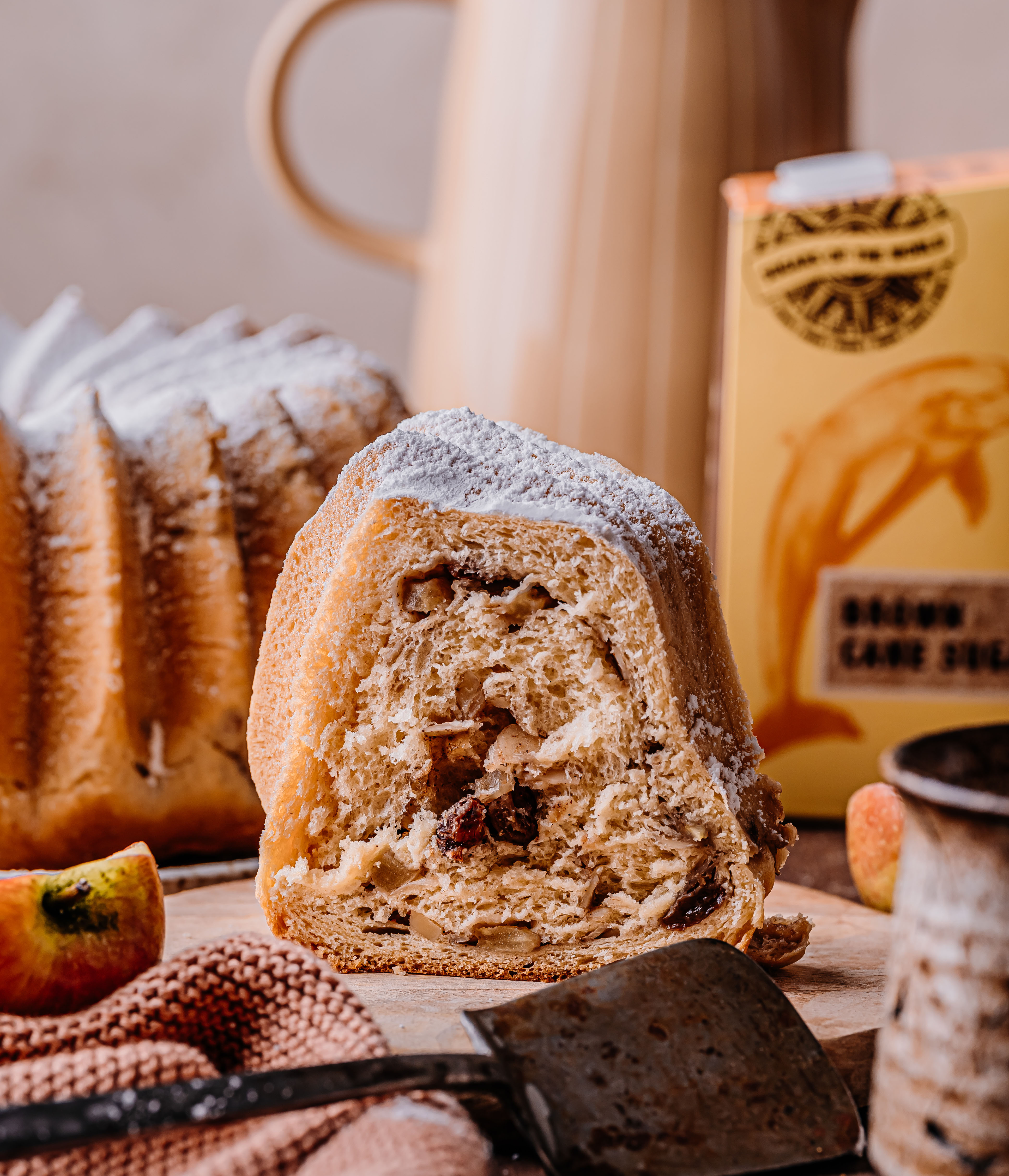 Ein Stück Gugelhupf mit Rosinen und Puderzucker, dahinter eine Packung brauner Rohrzucker