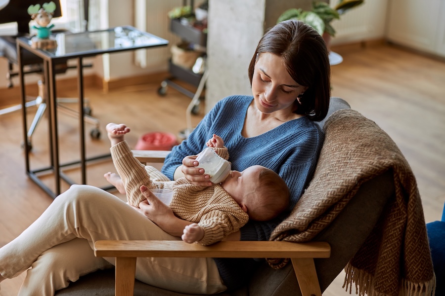 Mutter im Sessel gibt ihrem Baby im Wohnzimmer das Fläschchen