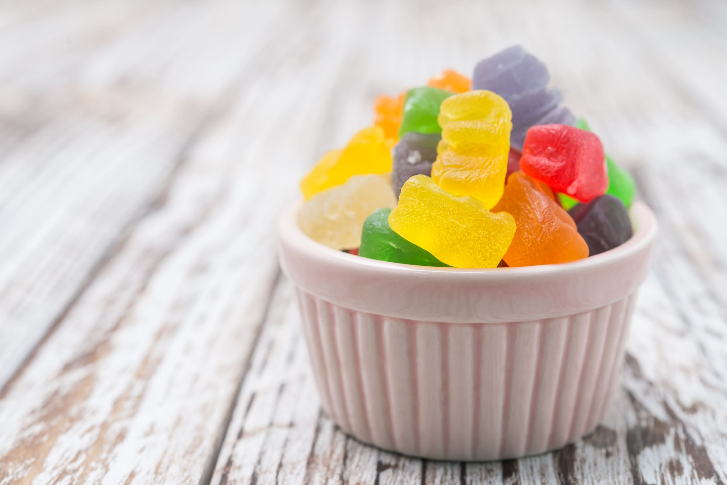 Bunte Fruchtgummis in einer kleinen rosa Schale auf einem weißen Holztisch