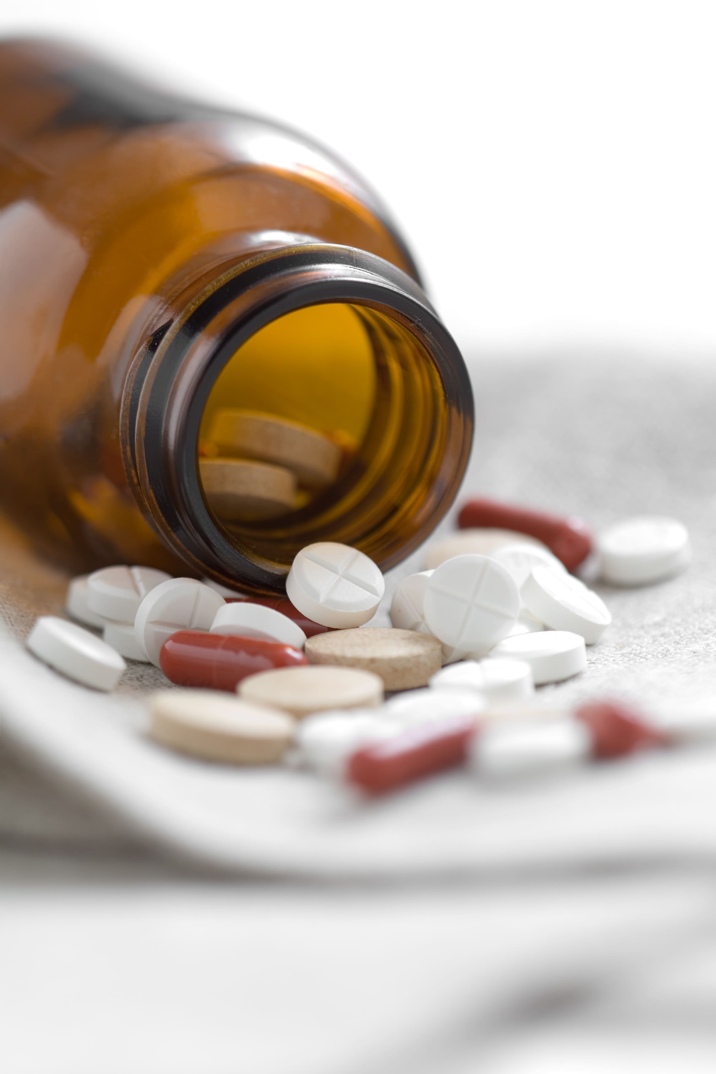 Weiße Tabletten und rote Kapseln fallen aus einer braunen Glasflasche