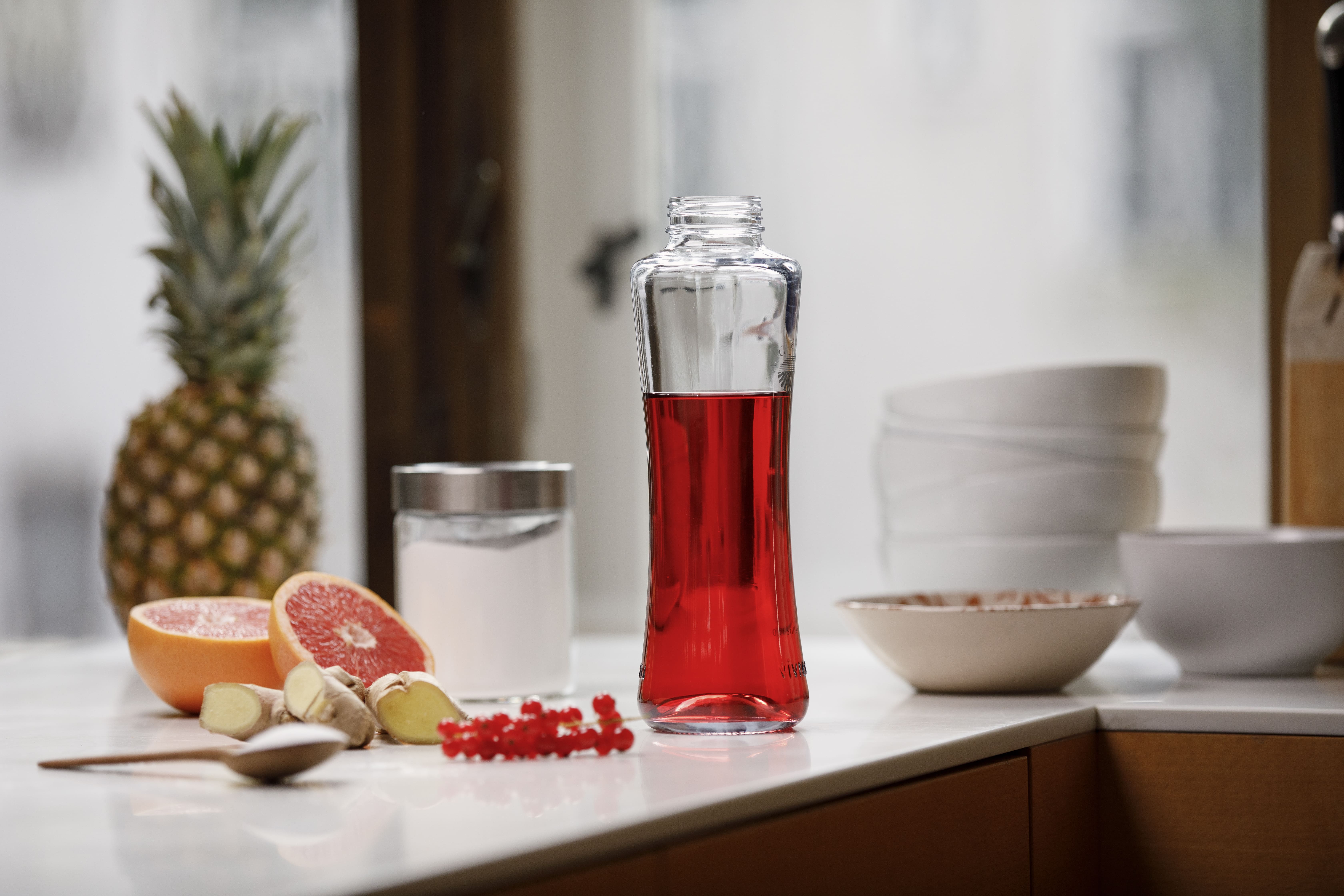 Flasche mit rotem Getränk auf einer Küchenzeile mit Ananas, Grapefruit, Ingwer und Ribiseln