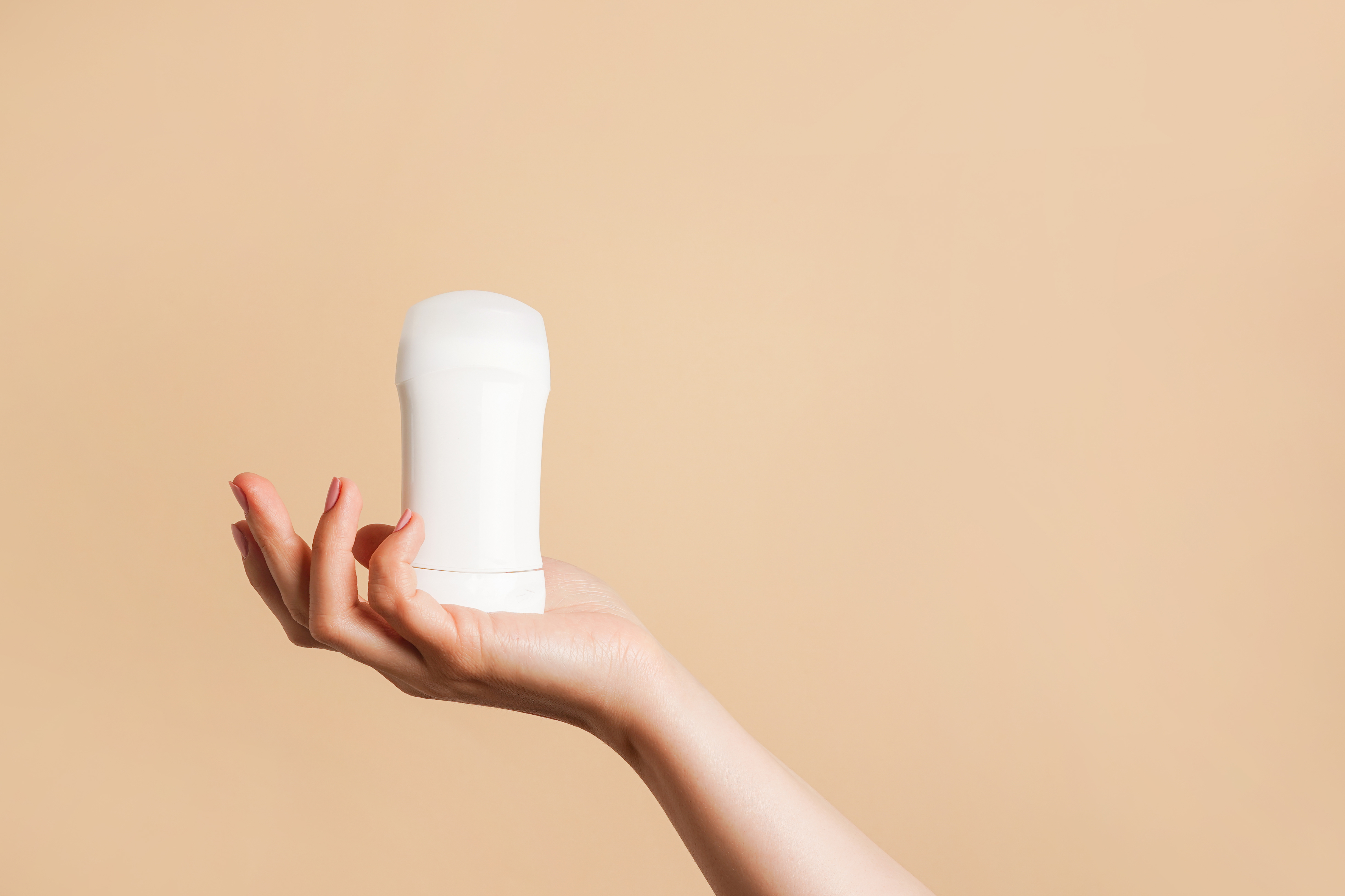 Hand hält einen weißen Deostick vor beigem Hintergrund