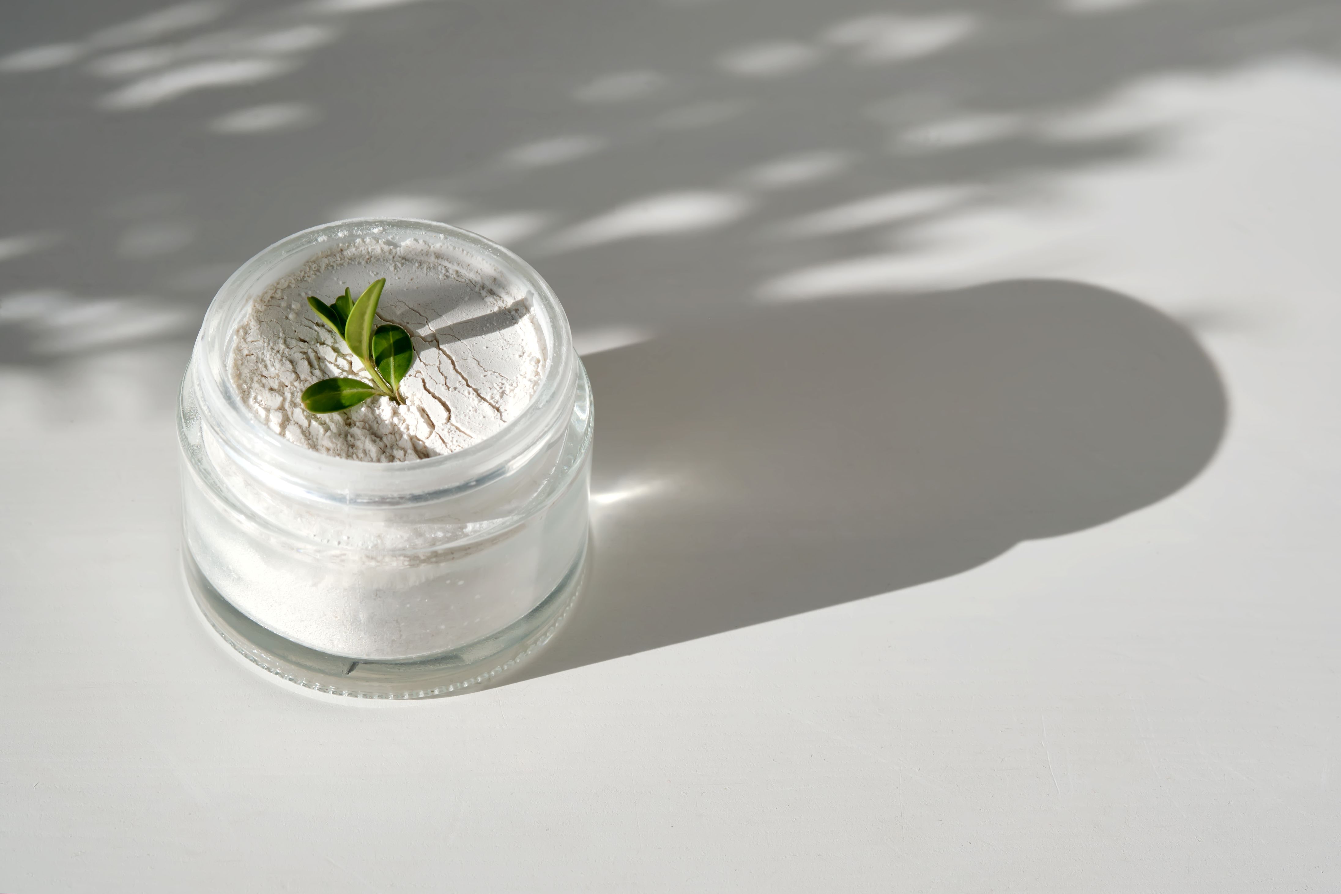 Glass jar of white powder peeling with a green leaf on top in dappled sunlight