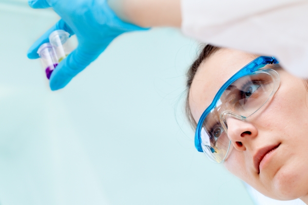 Laborantin mit Schutzbrille und blauen Handschuhen prüft kleine Probengefäße