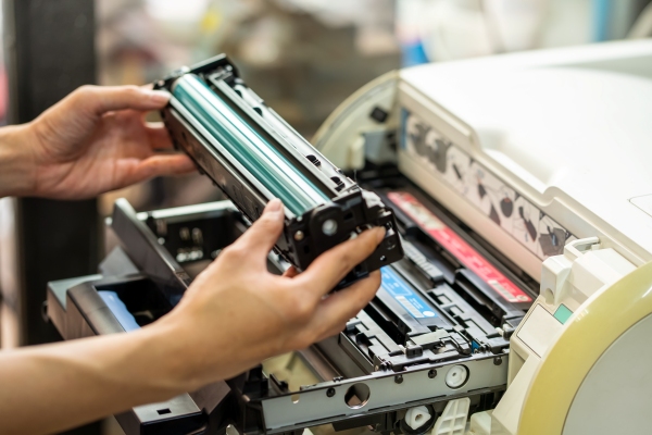 Hände setzen eine Tonerkartusche in eine Druckmaschine ein