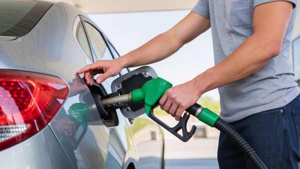 Man refuelling a silver car with a green fuel pump nozzle