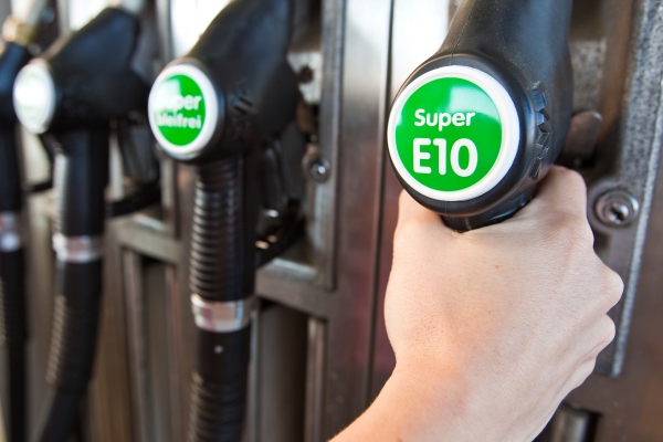 Hand grabbing a fuel pump nozzle labelled Super E10 at a petrol station
