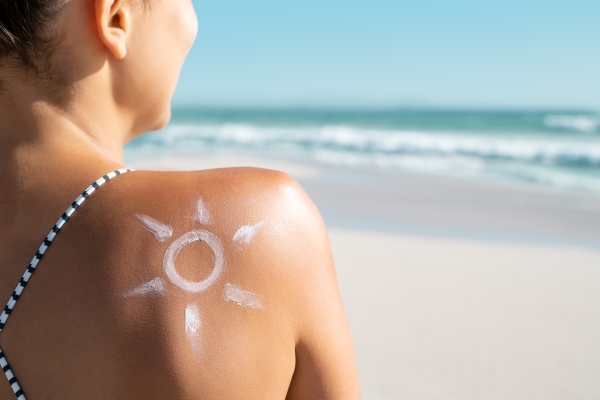 Sun drawn in sunscreen on a woman's shoulder at the beach with the sea behind