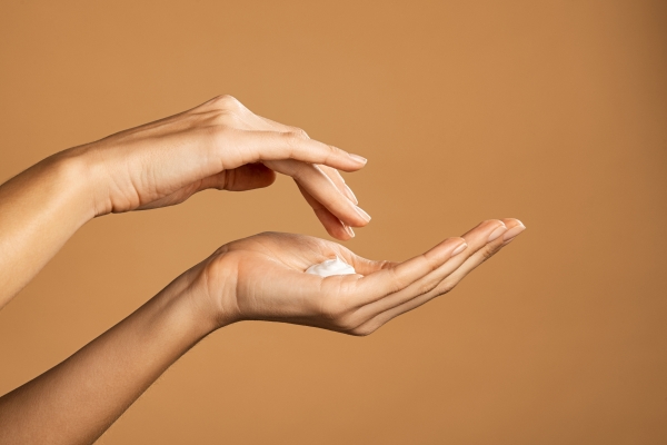 Two hands with a dab of white cream in the open palm against a beige background