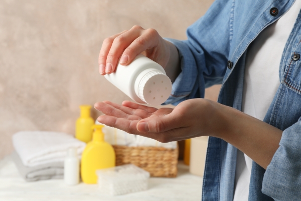 Person im Jeanshemd schüttet Babypuder aus einer weißen Flasche in die Hand