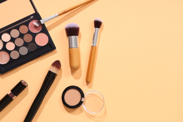Lidschattenpalette, Make-up-Pinsel, Kompaktpuder und Lippenstift auf pfirsichfarbenem Hintergrund