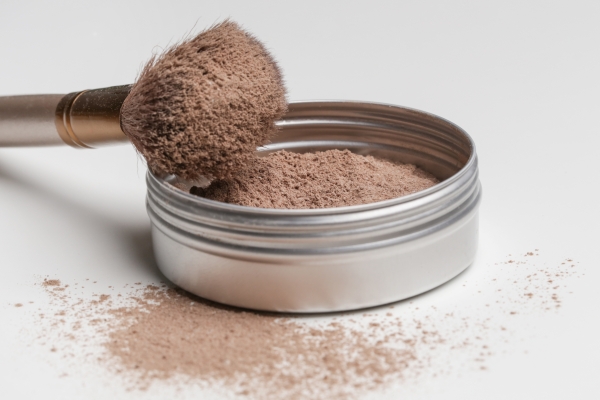 Make-up-Pinsel mit braunem Puder auf einer offenen Metalldose mit losem Puder