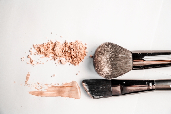 Swatches of loose powder and liquid foundation next to two makeup brushes on a white surface