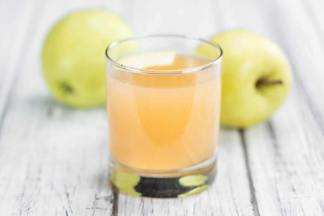 Glas naturtrüber Apfelsaft zwischen zwei grünen Äpfeln auf einem weißen Holztisch