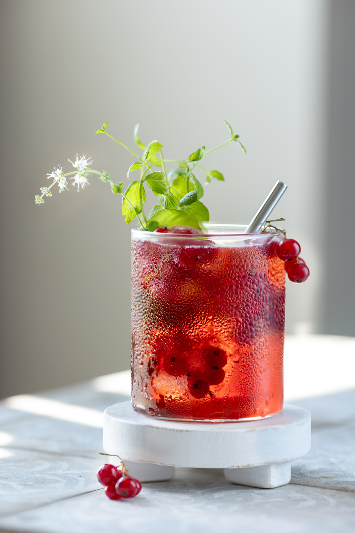 Glas Ribisel-Drink mit Eis, Minze und Strohhalm auf einem kleinen weißen Podest