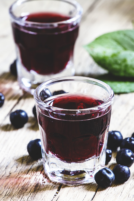 Zwei Gläser dunkelroter Beerensaft mit frischen Heidelbeeren auf einem rustikalen Holztisch
