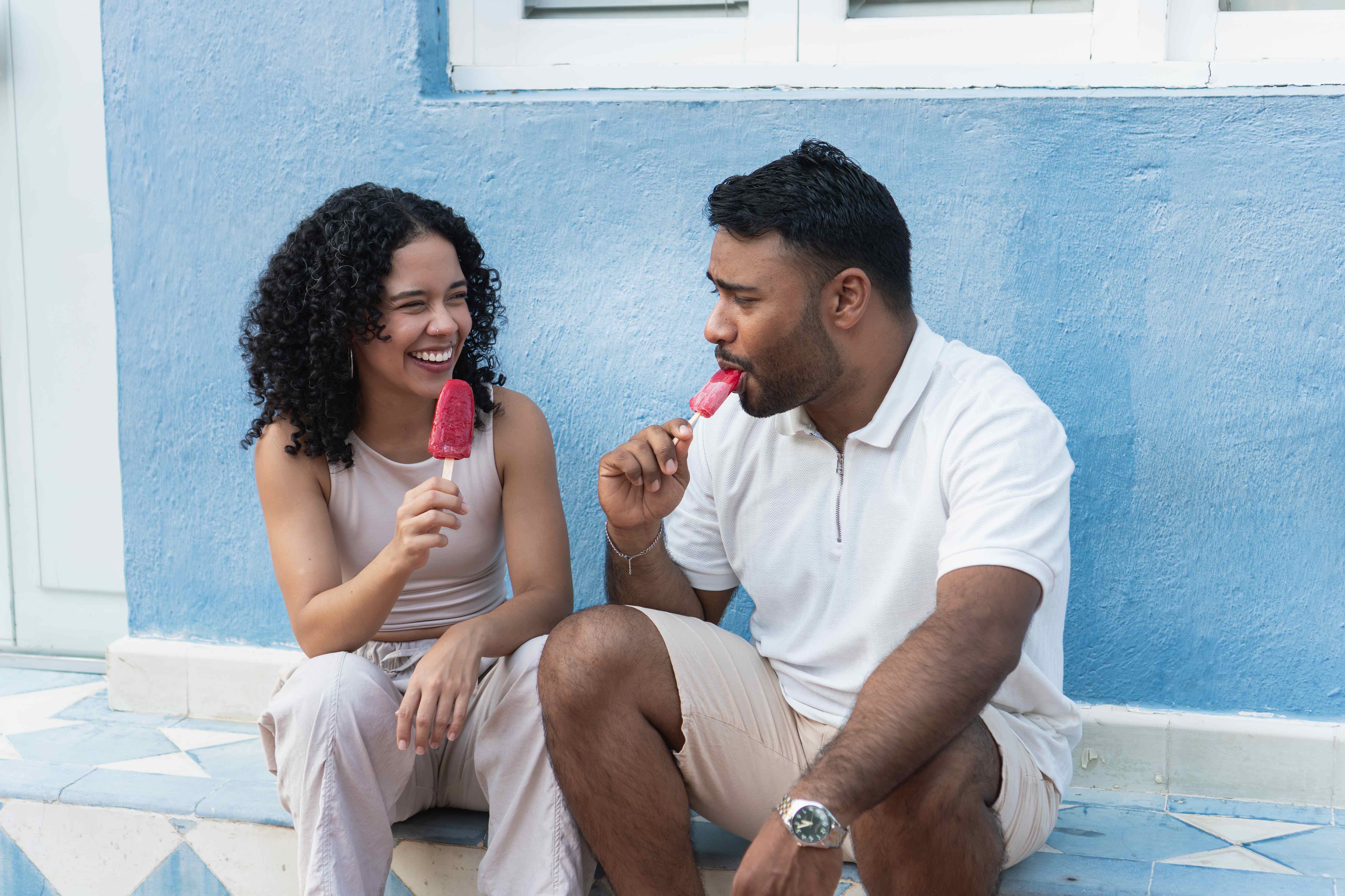 Zwei Frauen lachen und genießen Eis in Waffeln mit bunten Streuseln vor sommerlichem Himmel. [no AI]