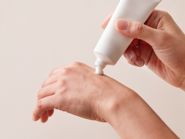 Hands squeezing white lotion from a tube onto the back of a hand