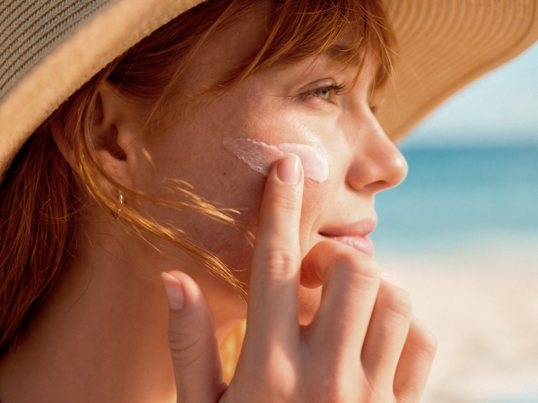 Woman in a straw hat applying sunscreen to her cheek at the seaside