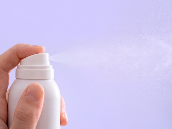 Hand spraying a white deodorant can against a lilac background