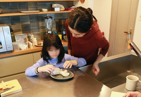 A mother is looking over the shoulder of her daughter eating fruits while having a conversation at the kitchen table