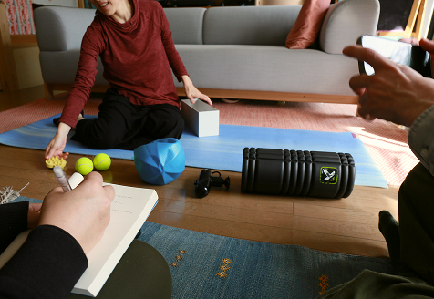 A woman is doing yoga in her loving room as a Japan immersion guide and observer take notes on her wellness routine