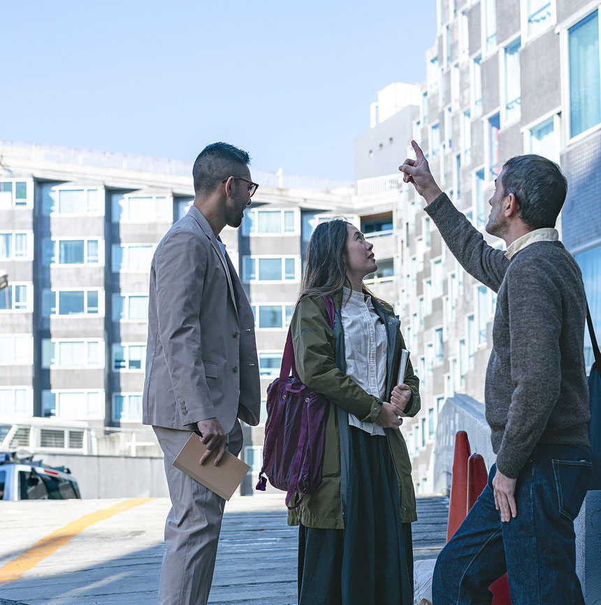 A photo of a guide pointing and explaining the history of a Harajuku vintage apartment on the right. On the left two designers are listening to the history of the building.
