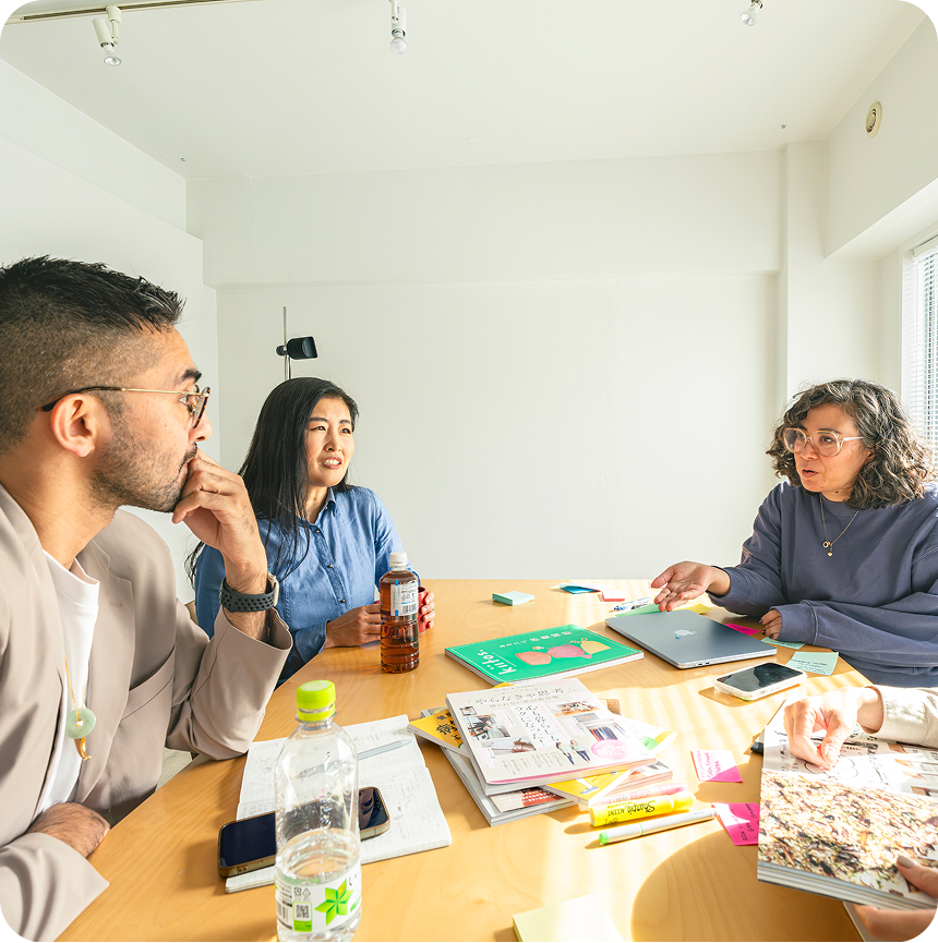 A photo of 3 people brainstorming planning at a table with notebooks, pens and a waterbottle