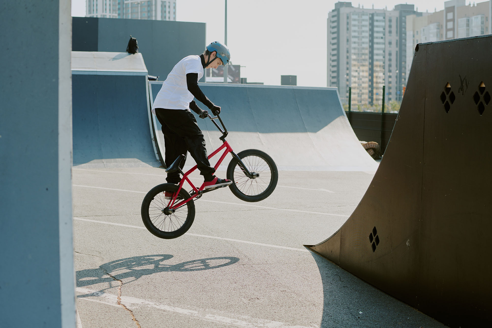 Person mit Helm, die auf einem roten Fahrrad in einem Skatepark einen BMX-Sprungtrick ausführt.