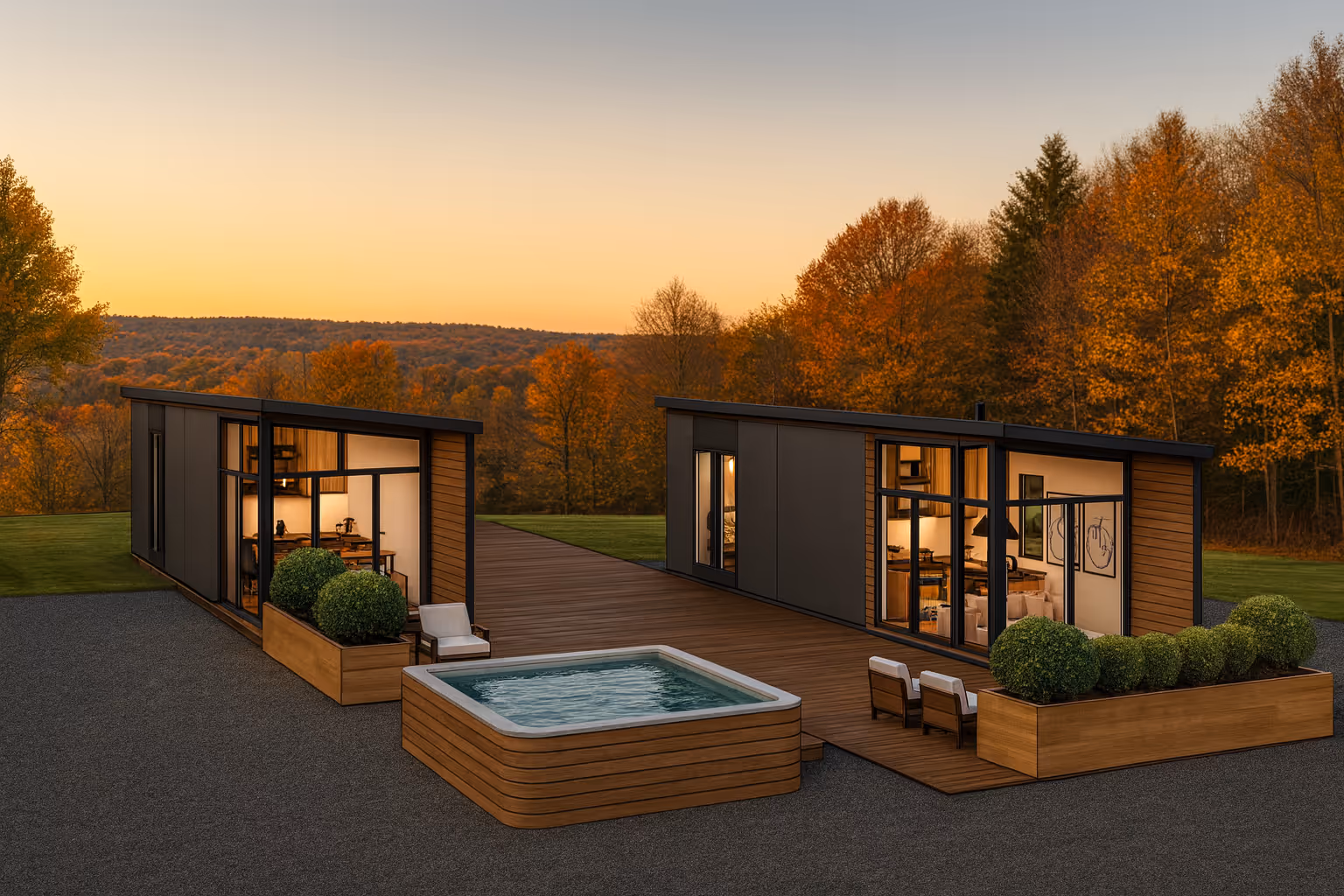 Two modern single-story homes with large windows connected by a wooden deck, featuring a hot tub and outdoor seating, set against autumn trees at sunset.