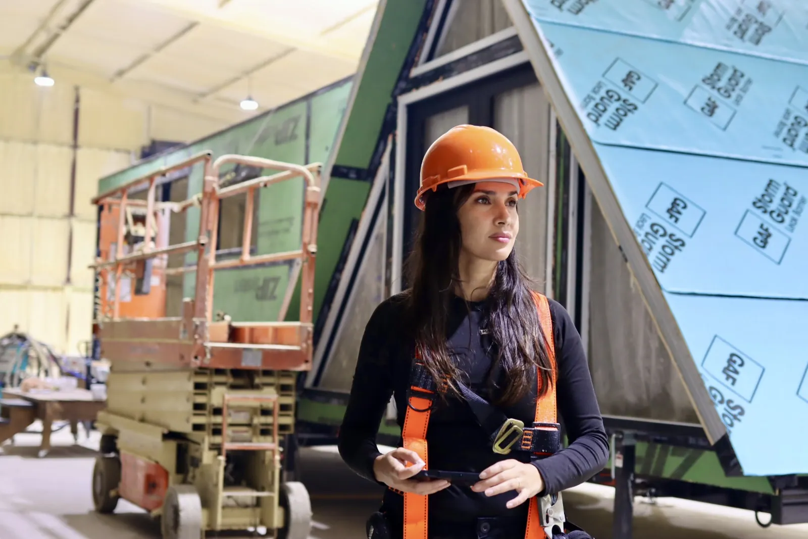 Founder Anabella Mainetti in a hard hat in front of an A-frame tiny home under construction in the Mainefactured facility