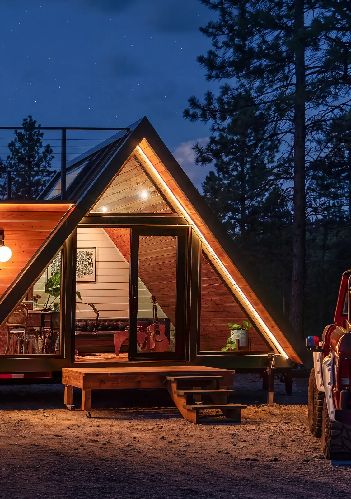 Casa Francesca A-frame tiny home at night, glowing with warm light, a guitar visible inside