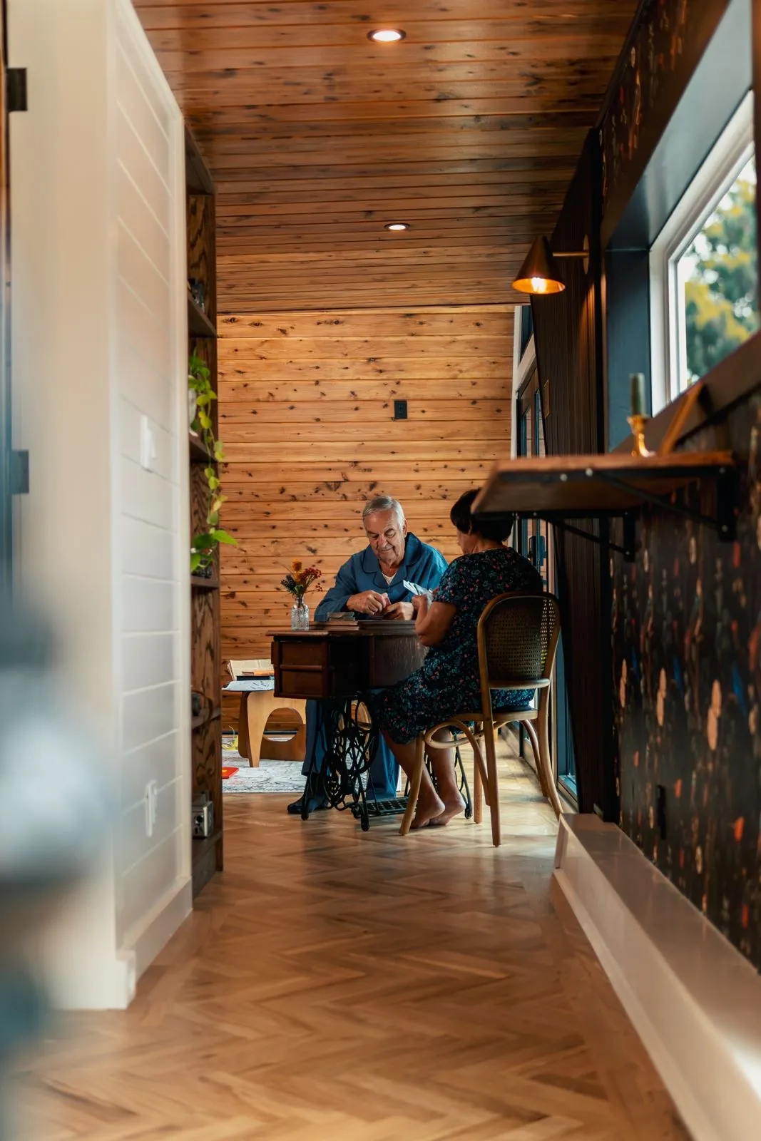 Older couple seated at a table in a hallway with a cedar ceiling inside a Mainefactured tiny home