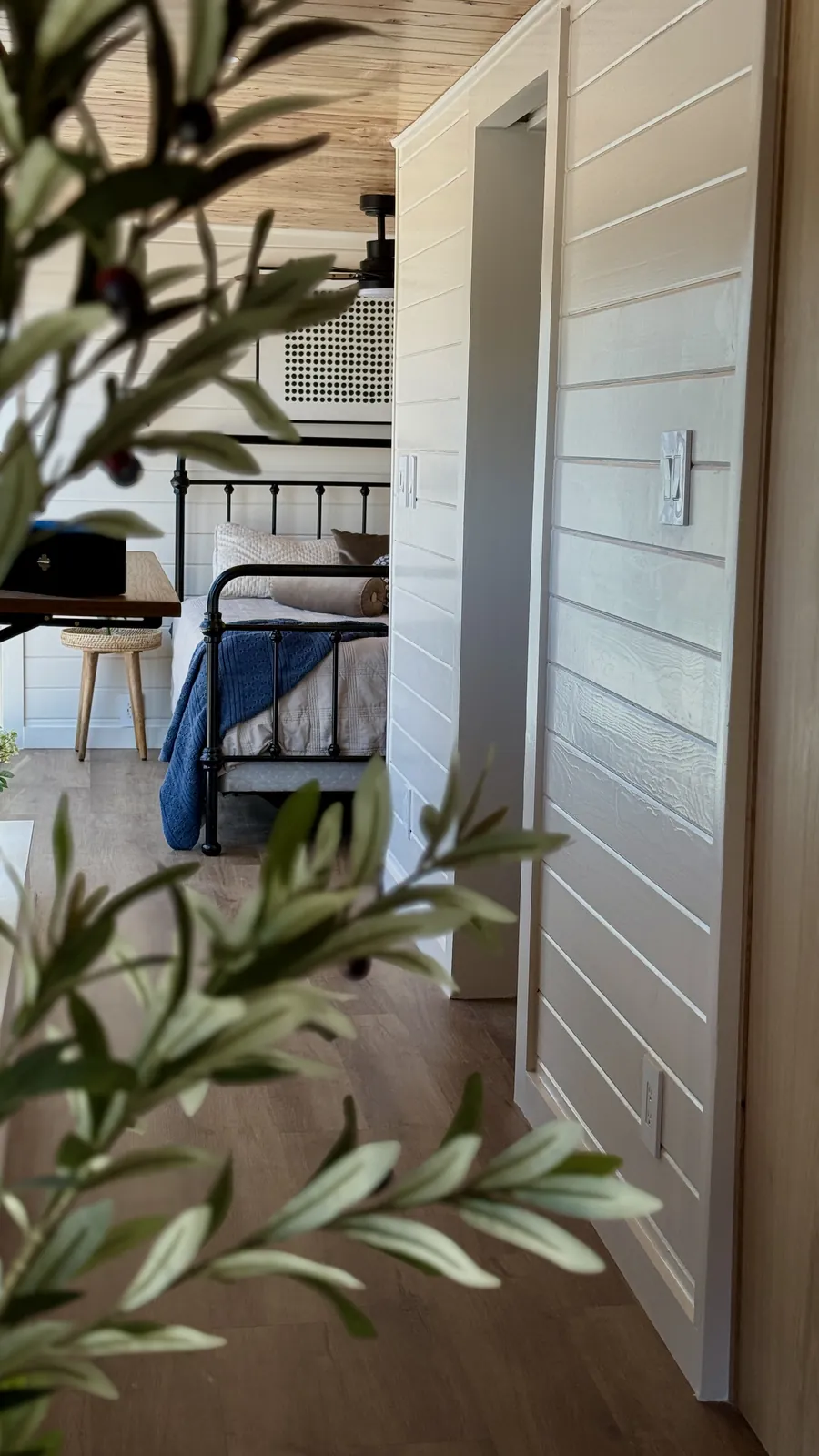 Bedroom seen past olive branches in a Mainefactured tiny home