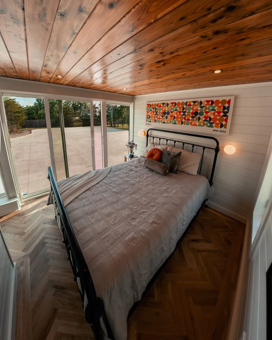 Bedroom with Bauhaus art above an iron bed and herringbone wood floors