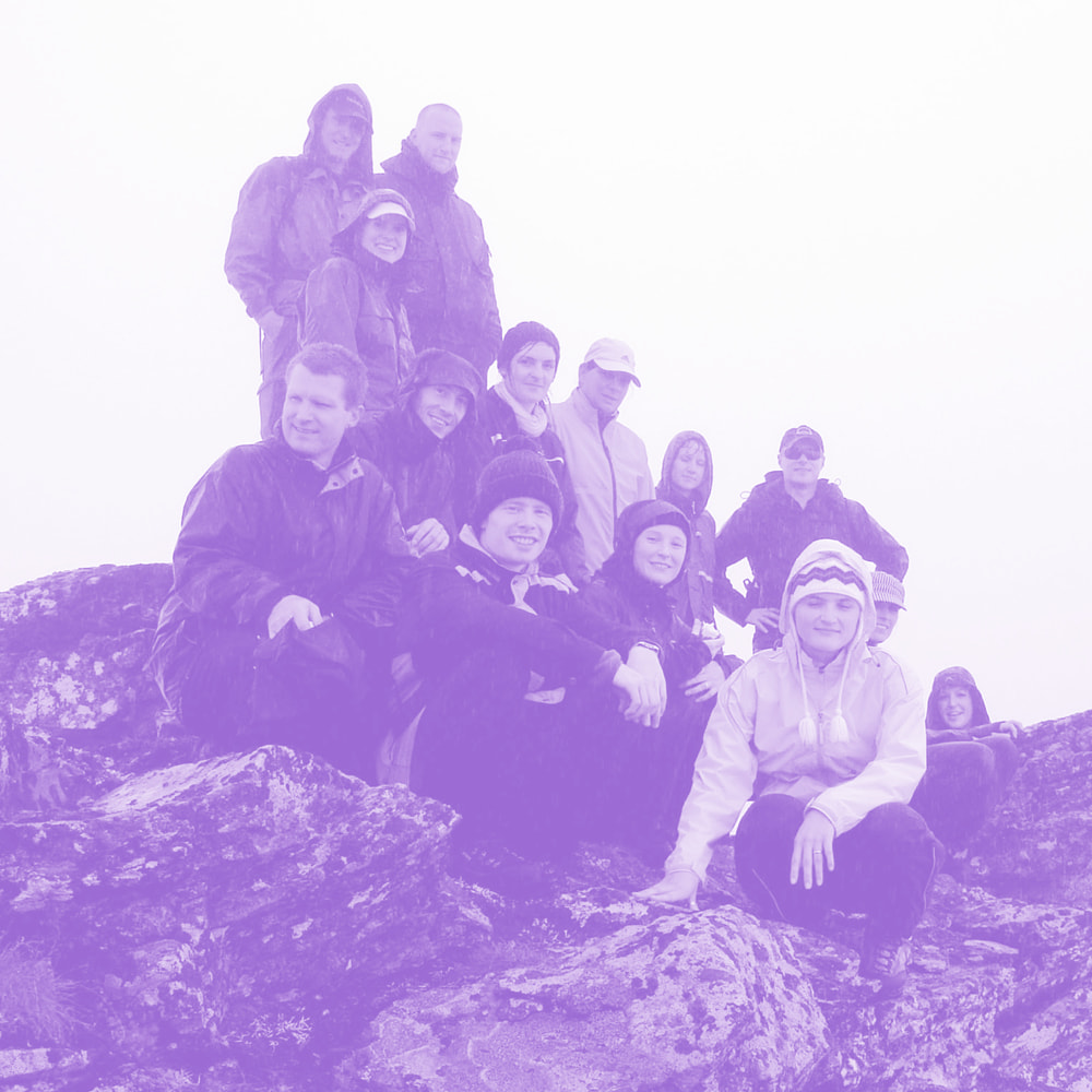 Group of people dressed in outdoor gear sitting and standing on rocky terrain, posing for a photo in overcast weather.