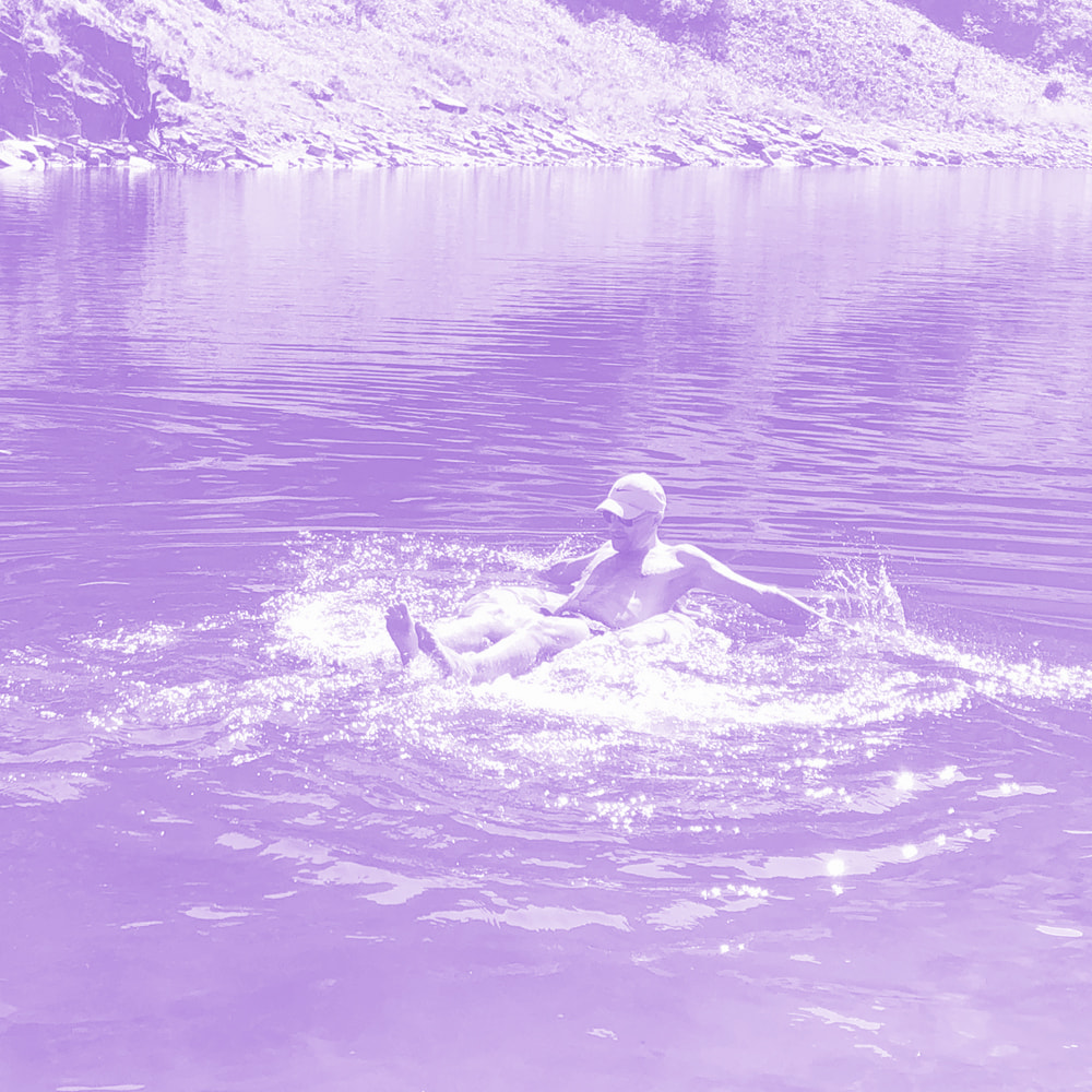 Person wearing a cap splashing in a calm lake near a rocky shore.