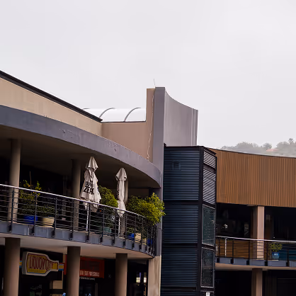 Modern commercial building with balconies, outdoor umbrellas, and metal railings under a cloudy sky.
