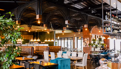 Interior of a modern restaurant with mixed seating, hanging pendant lights, and large windows.