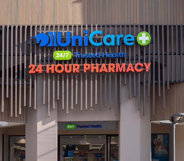 Storefront of UniCare 24/7 Trusted Health with a large sign reading '24 HOUR PHARMACY' on a modern building facade.
