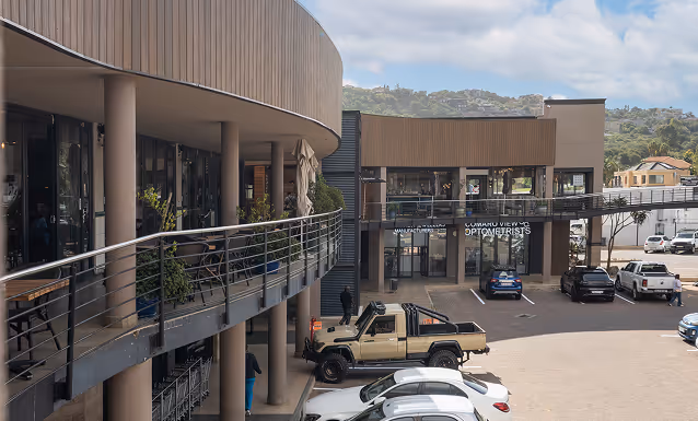 Outdoor view of a modern shopping complex with parked cars and a balcony with railings on the left side.