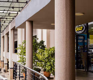 Outdoor shopping area with columns, potted plants, and a store sign reading 'KRAZY'.