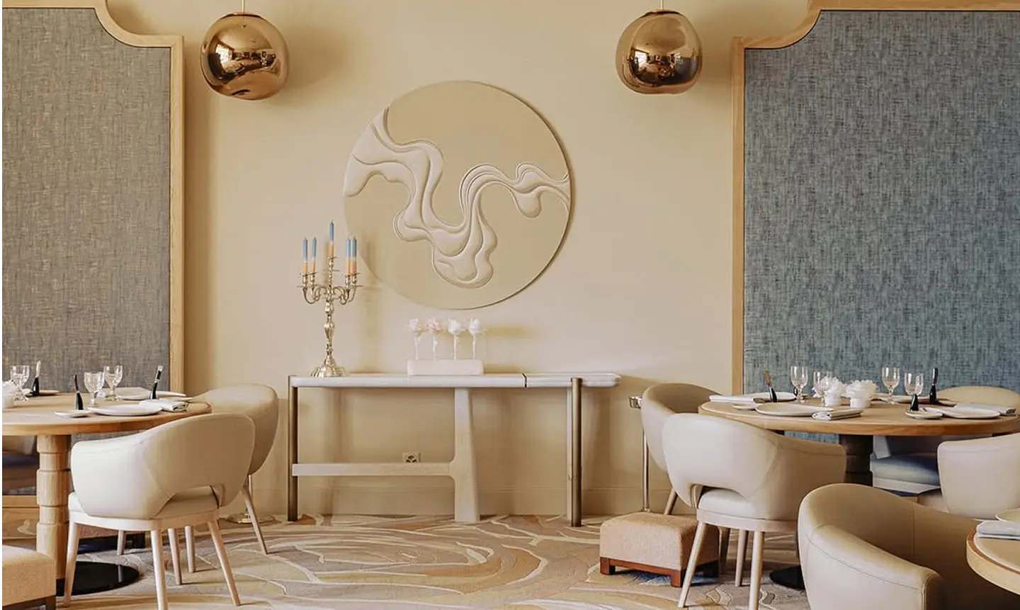 Intérieur élégant de restaurant avec tables rondes en bois, chaises beige, lustres dorés suspendus et décoration murale artistique.