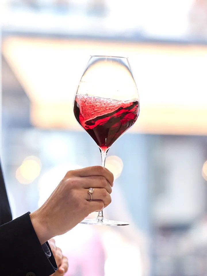 Main tenant un verre de vin rouge en train d'être agité avec éclaboussures visibles dans le verre.